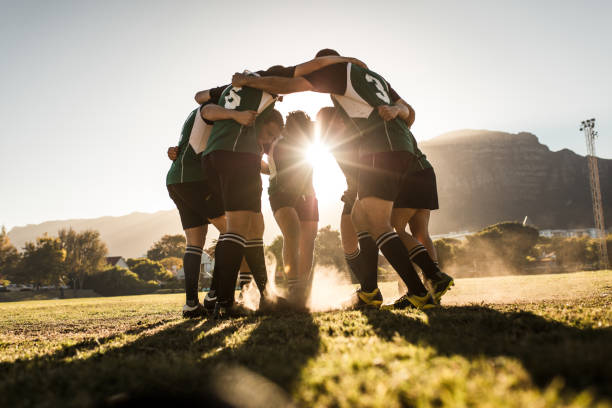 Rugby team standing in a huddle and rubbing their feet on ground. Rugby team celebrating victory.